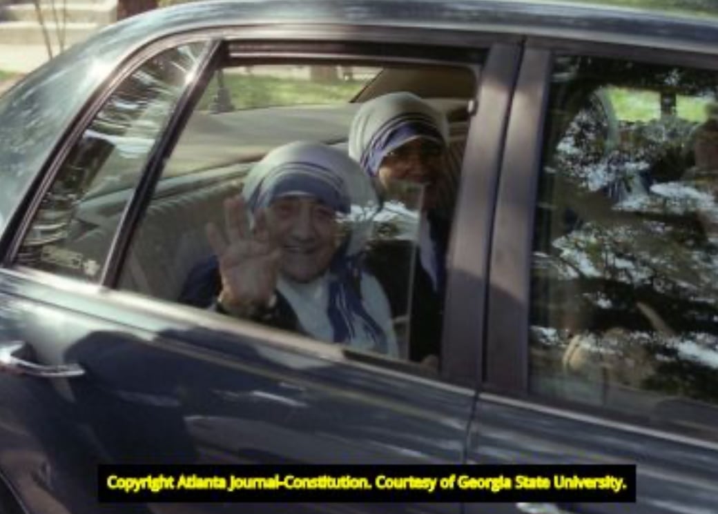 two women with religious veils wave from the backseat of a car